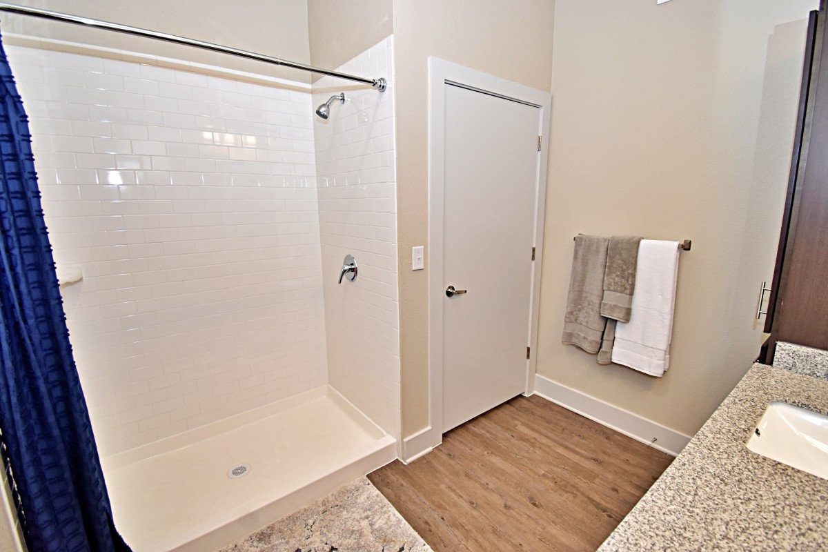 A modern bathroom with a spacious shower, white door, and neatly hung towels.