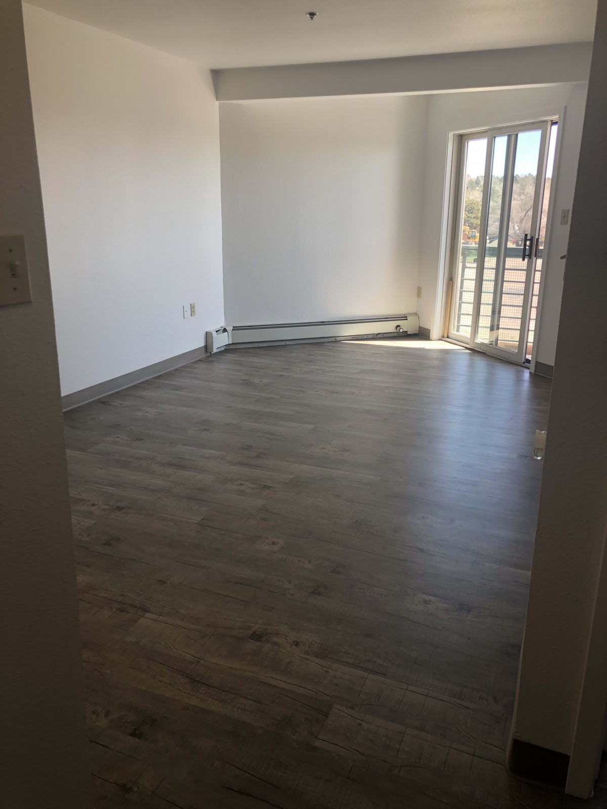 A bright, empty room with hardwood floors and large windows allowing natural light.