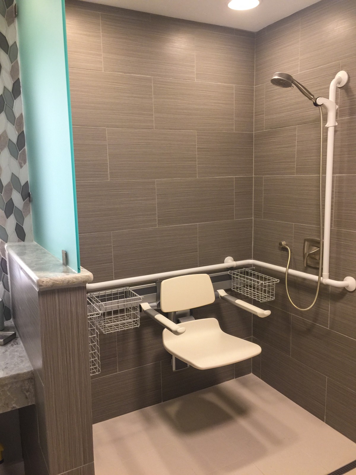 A bathroom featuring an accessible walk-in shower with a foldable seat and safety rails.