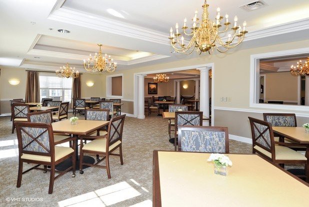 A spacious and elegant dining room featuring multiple tables, chairs, and golden chandeliers.