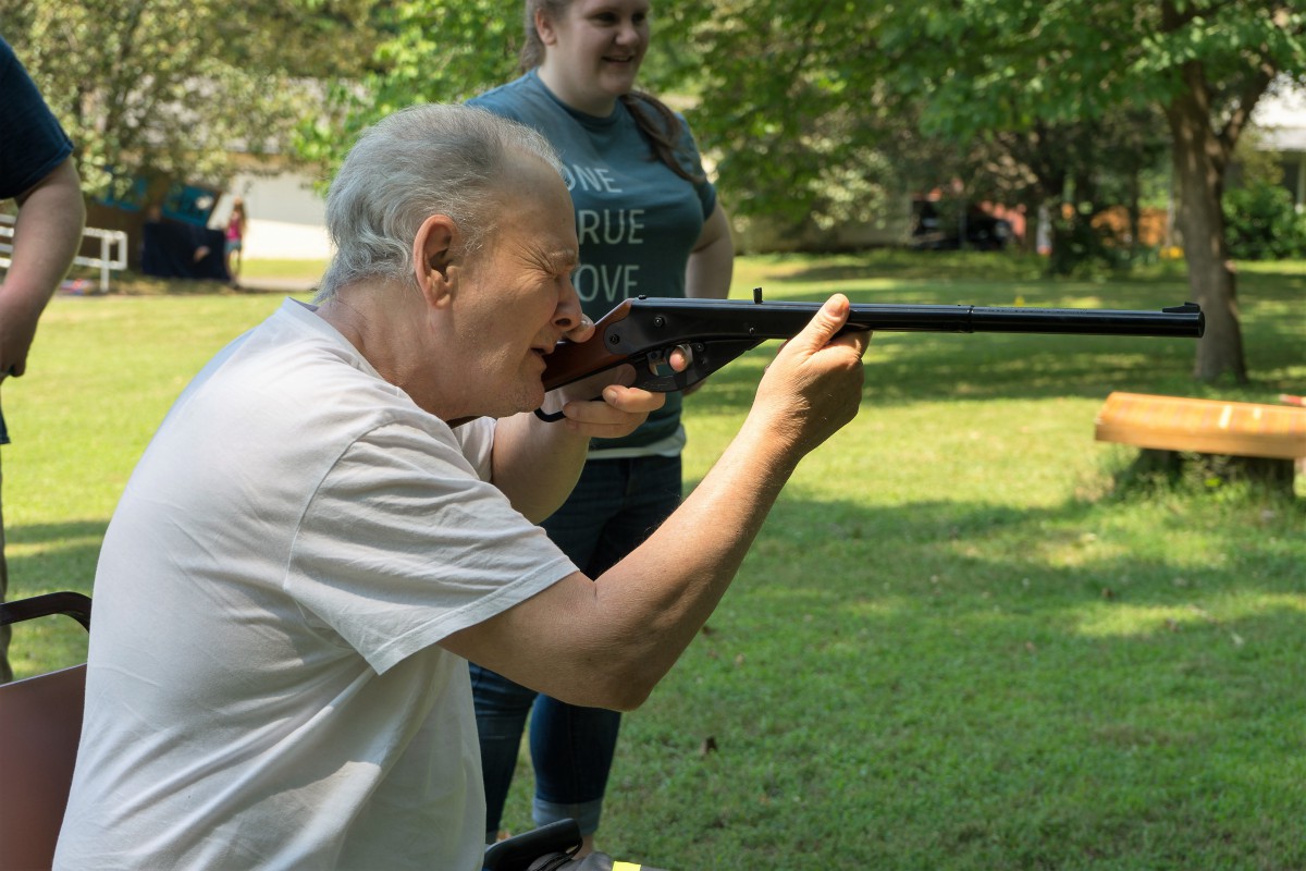 An elderly person aiming a rifle outdoors during a recreational activity.