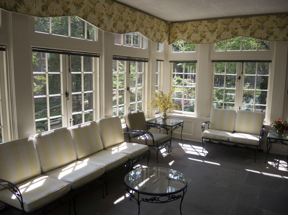 A bright sunroom filled with natural light, featuring comfortable seating and glass tables.