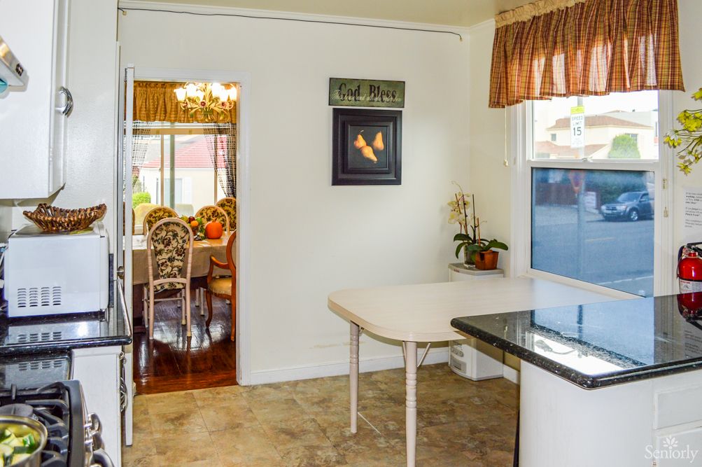 A view from a kitchen looking into a dining area, featuring a small table, chairs, and decor.