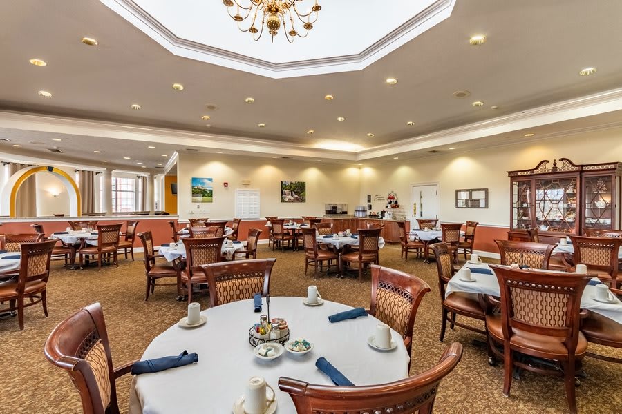 A spacious dining area with elegantly set tables and a chandelier overhead.