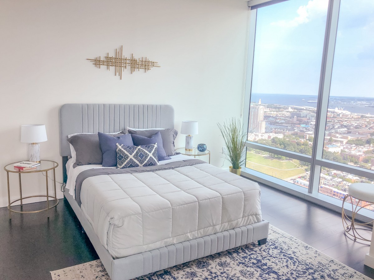 A modern bedroom with a large window offering a city view, featuring a stylish bed and chic decor.