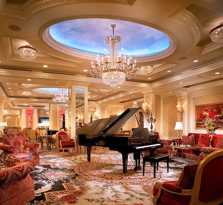 A lavish hotel lobby featuring a grand piano, ornate chandeliers, and luxurious decor.