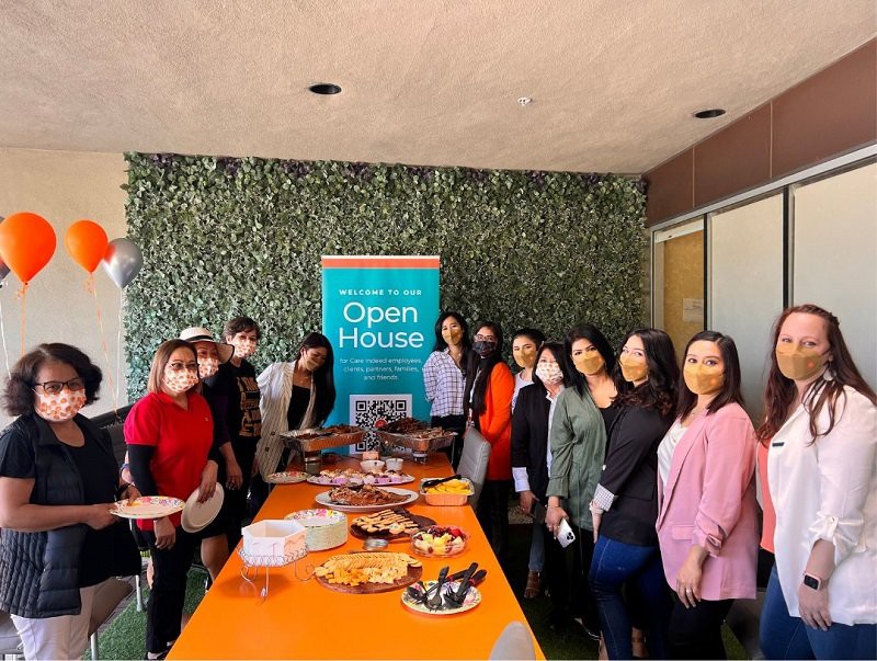 A group of women gathered around a table with food at an open house event.