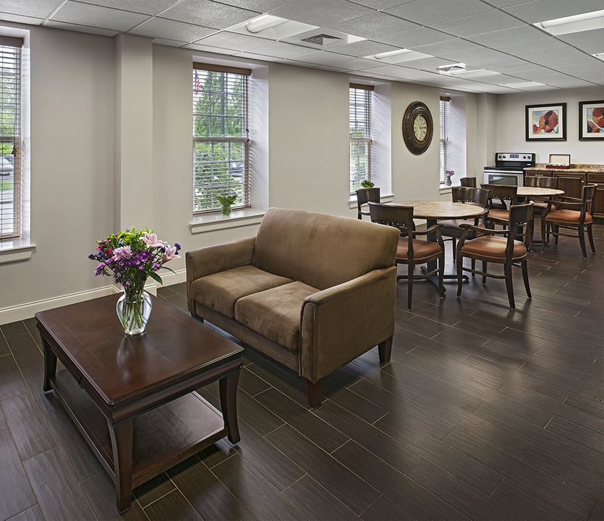 A cozy waiting area with a couch and coffee table, featuring flowers and natural light from the windows.
