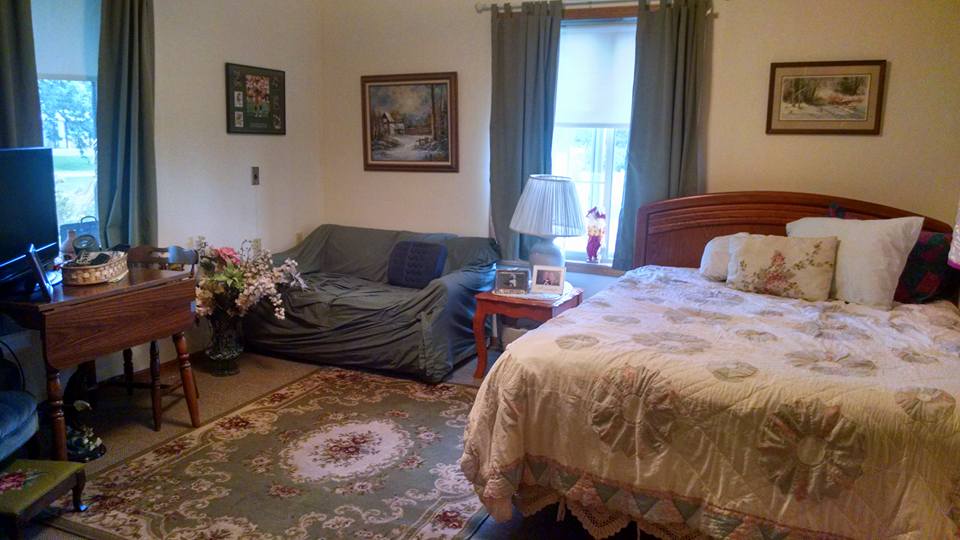 A cozy bedroom with a bed, sofa, and decorative elements such as paintings and a patterned rug.