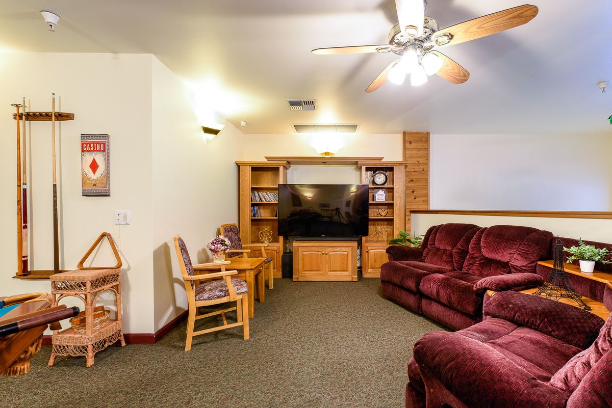 A cozy living room with a large television, comfortable seating, and wooden shelves.