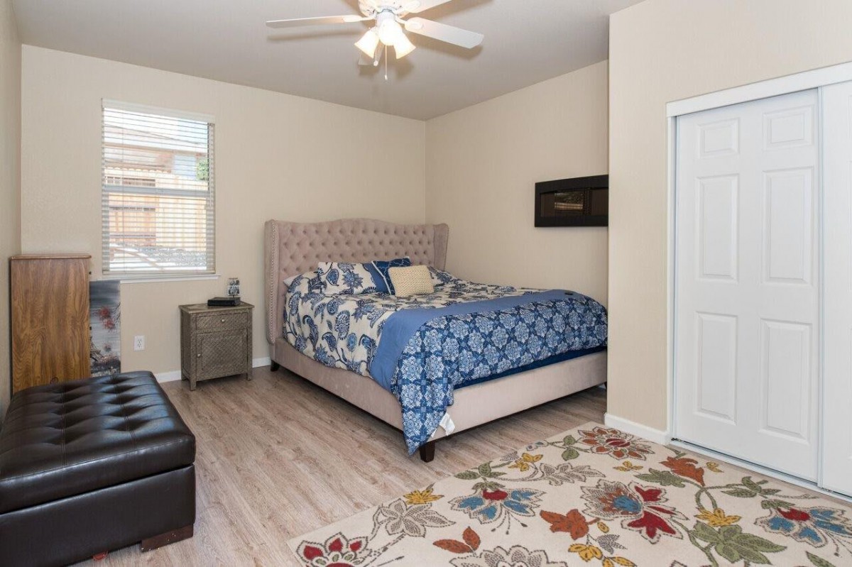 A cozy bedroom with a patterned bedspread, floral rug, and ceiling fan.