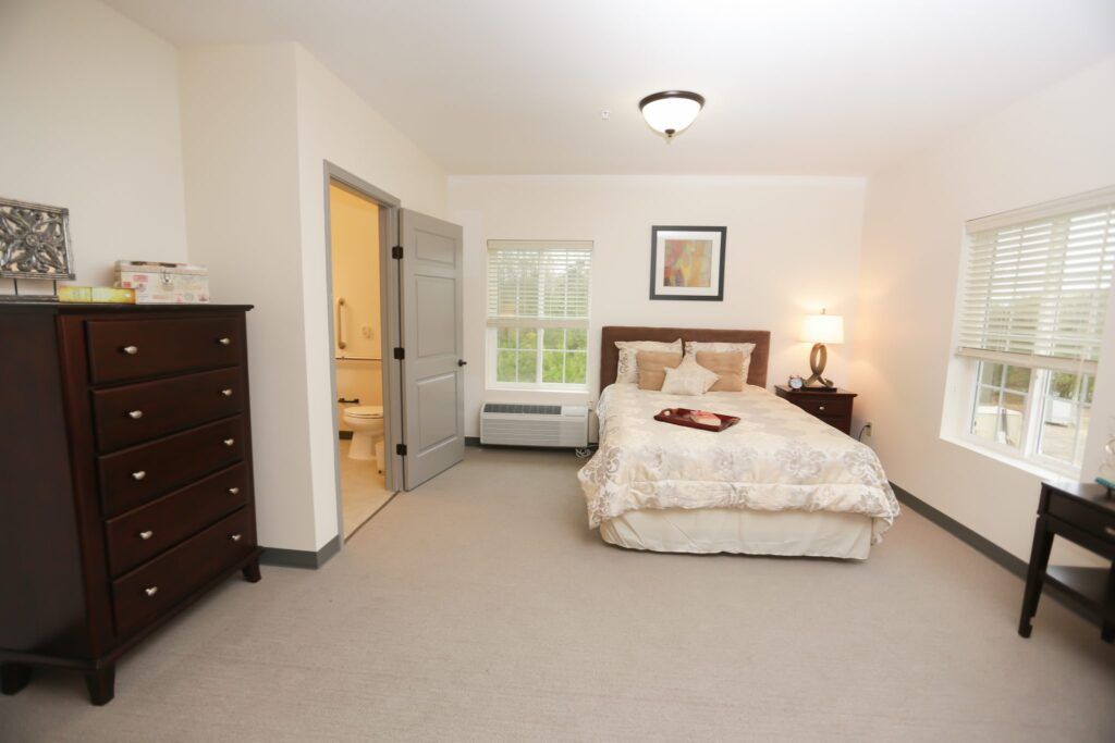A cozy bedroom with a bed, dresser, and a lamp by the window.