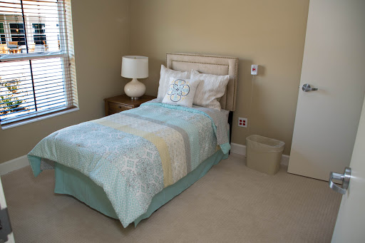 A cozy and calming bedroom featuring a single bed with decorative pillows, a lamp on a nightstand, and light-colored walls.