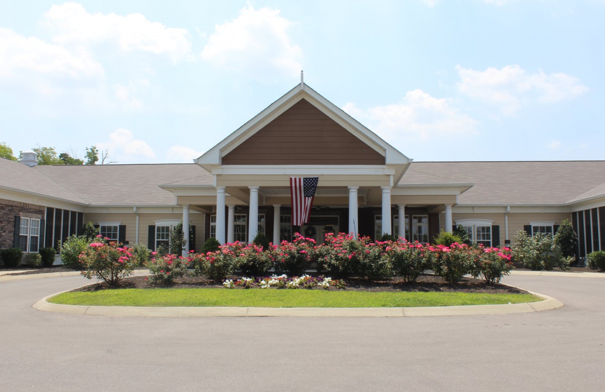 A suburban building entrance with landscaped flowers and a flagpole.
