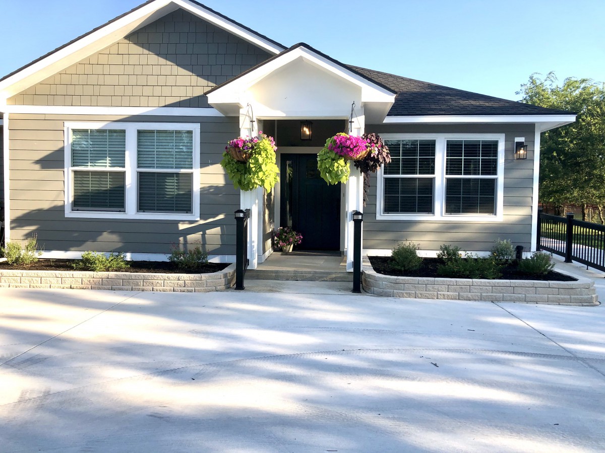 A charming bungalow with a well-maintained front yard and colorful hanging flower baskets, illuminated by the sun.