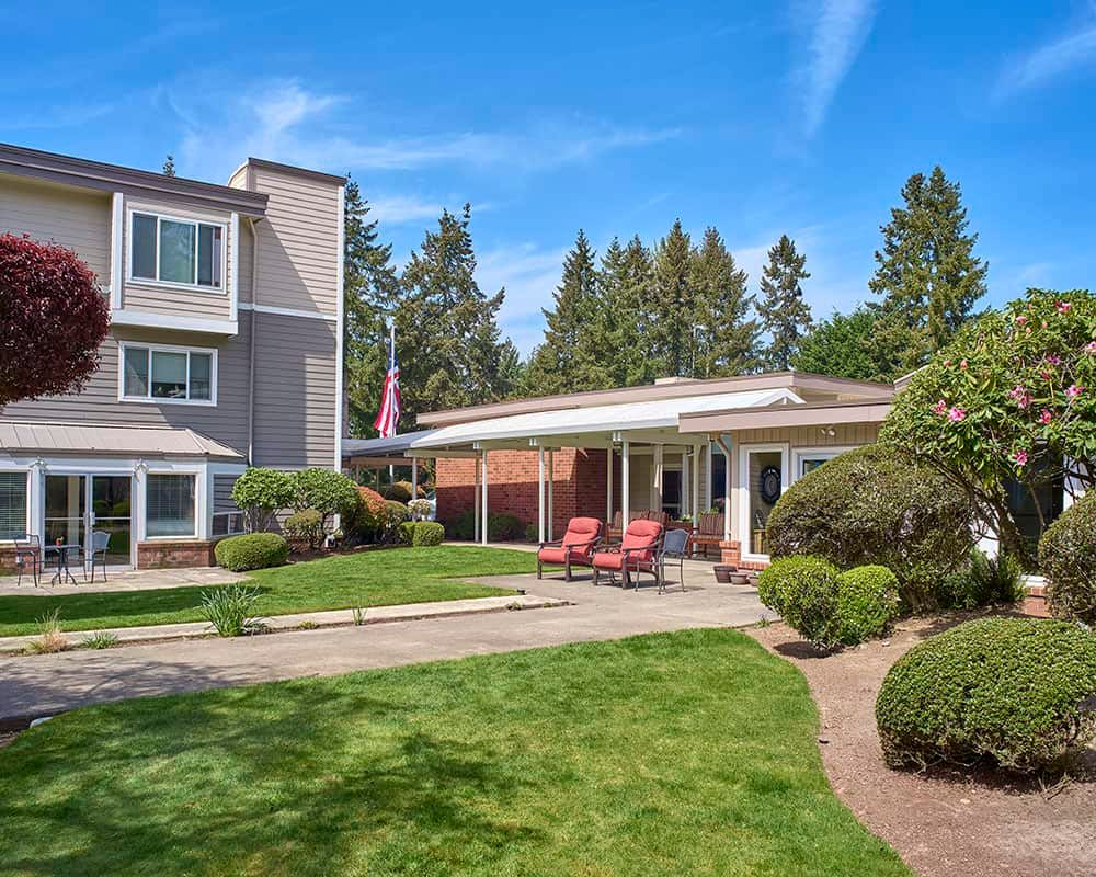 A well-maintained residential building with a manicured lawn and trees under a clear blue sky.