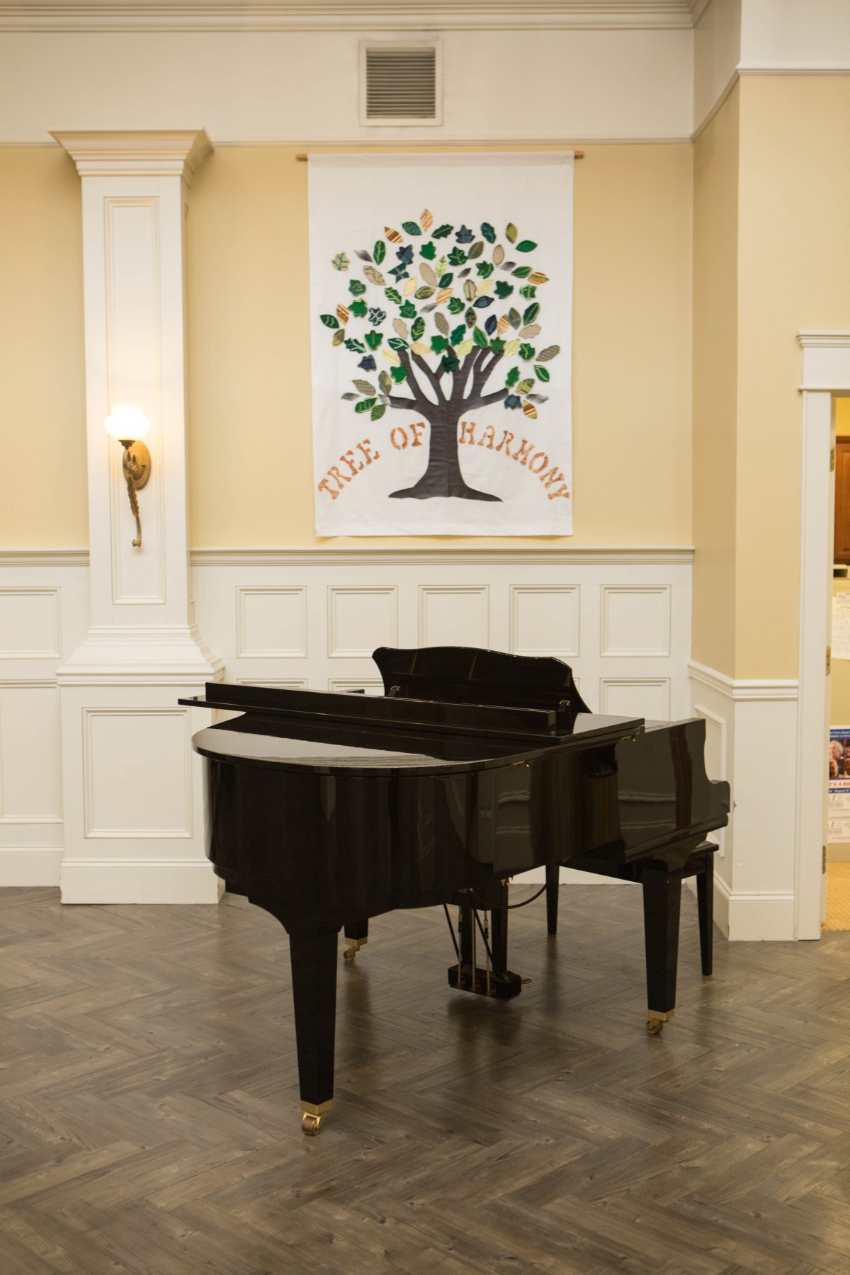A grand piano is placed in an elegantly decorated room featuring a tree-themed artwork on the wall.