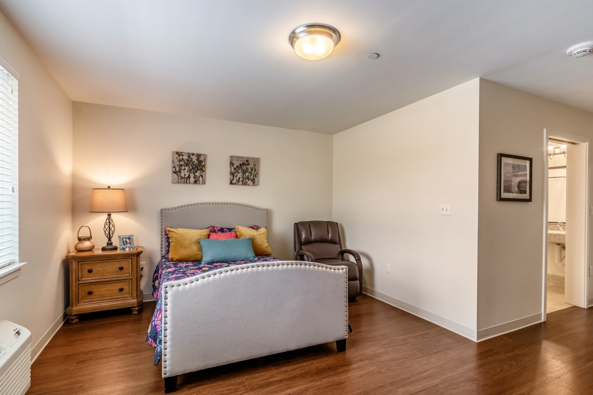 A cozy bedroom with a bed, bedside table, and chair on a hardwood floor.