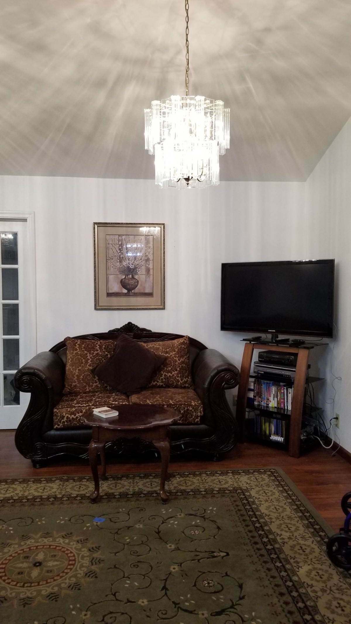 A cozy living room with a sofa, chandelier, and television.