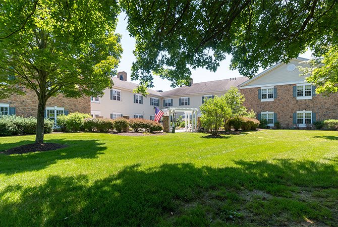 A residential building surrounded by a lush green lawn and trees under bright sunlight.
