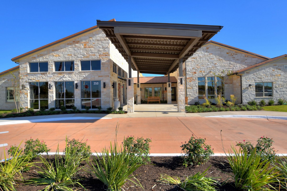 A modern building with a landscaped entrance and stone facade.
