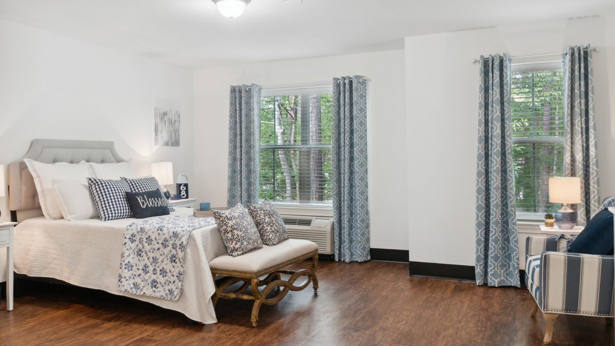 A cozy bedroom with a bed, patterned curtains, and hardwood flooring.