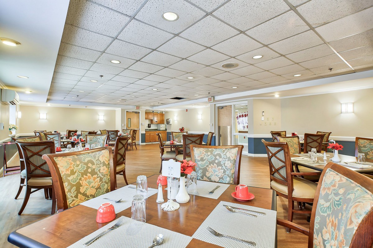 The image shows an empty restaurant dining room with neatly set tables and chairs.