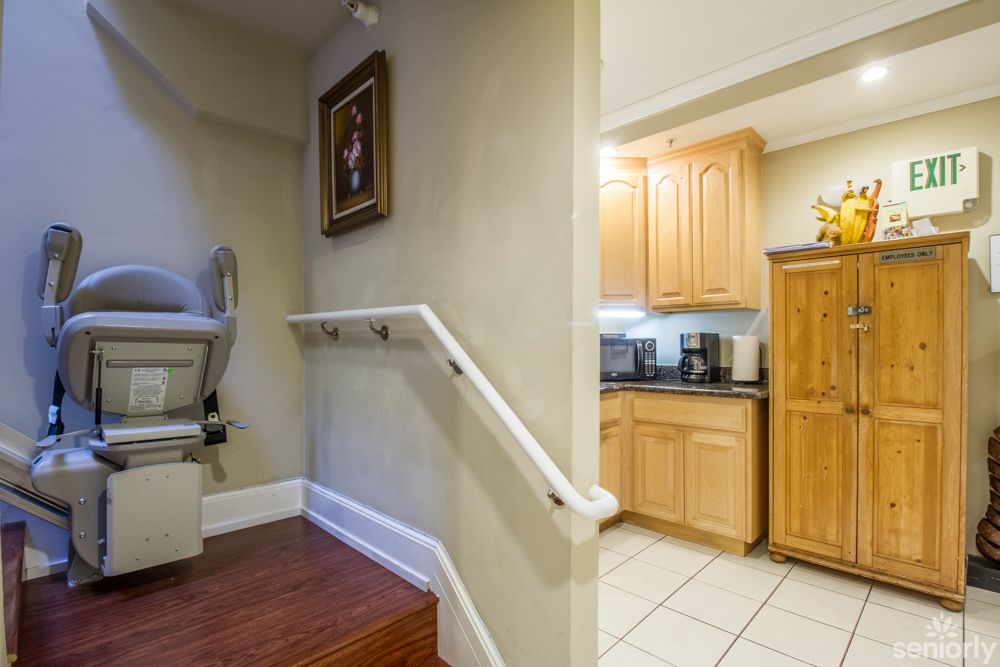 A cozy kitchen area next to a staircase equipped with a stairlift, featuring wooden cabinetry.