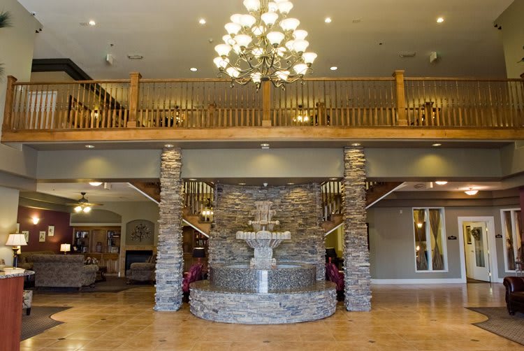 A spacious lobby featuring a stone fountain, elegant chandelier, and wooden balcony.