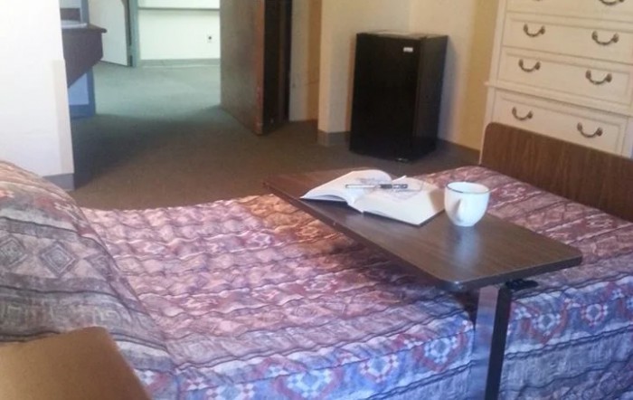 A cozy hotel room with a bed, small table, and a mini fridge.