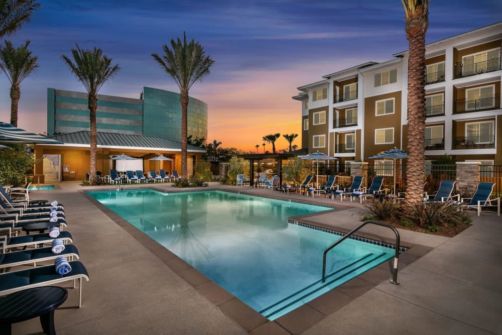 A beautiful apartment complex with a swimming pool surrounded by palm trees at sunset.