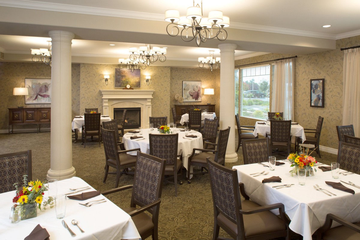 Elegant dining room with neatly arranged tables and chairs, featuring chandeliers and a fireplace.
