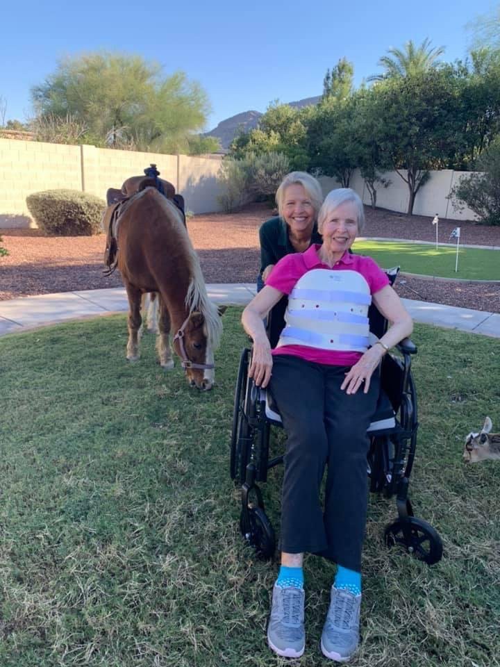 Two women outdoors with a horse grazing nearby.