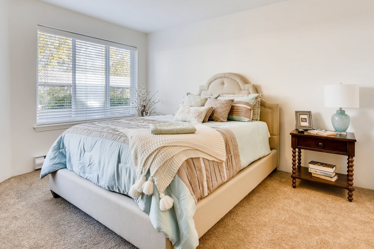 A cozy and well-lit bedroom featuring a neatly made bed with pastel-colored bedding.