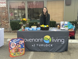 A representative from Covenant Living at Turlock stands behind a promotional table, ready to engage with the community at an outdoor event.