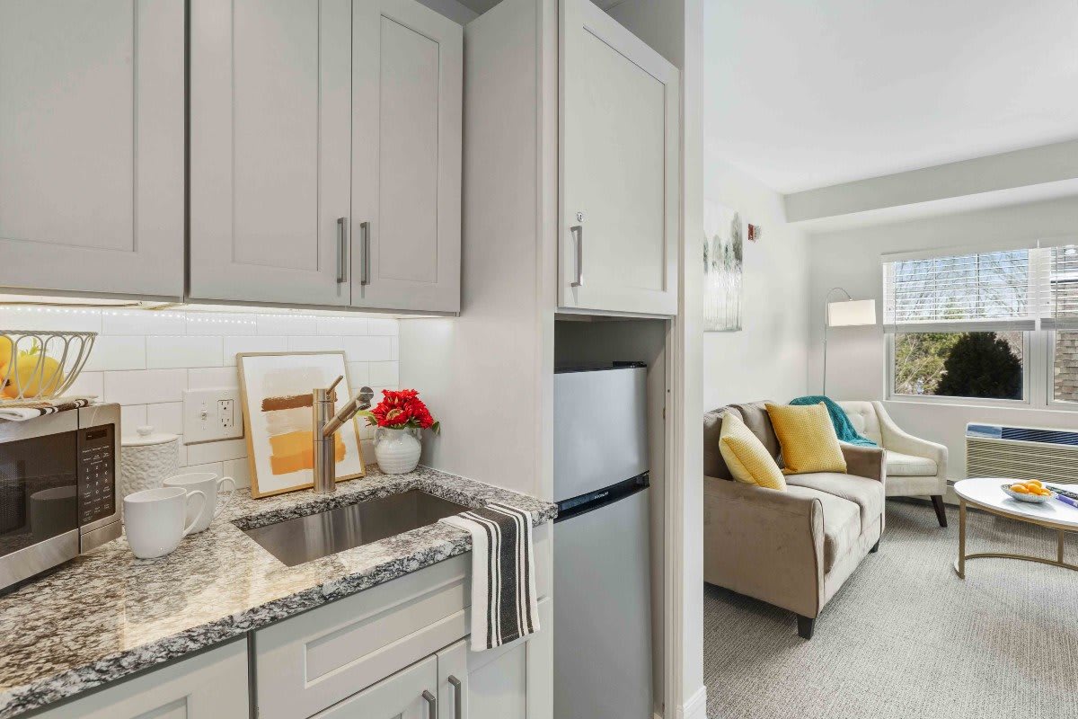 A modern apartment kitchen with adjacent living room, featuring stylish cabinetry and cozy seating.