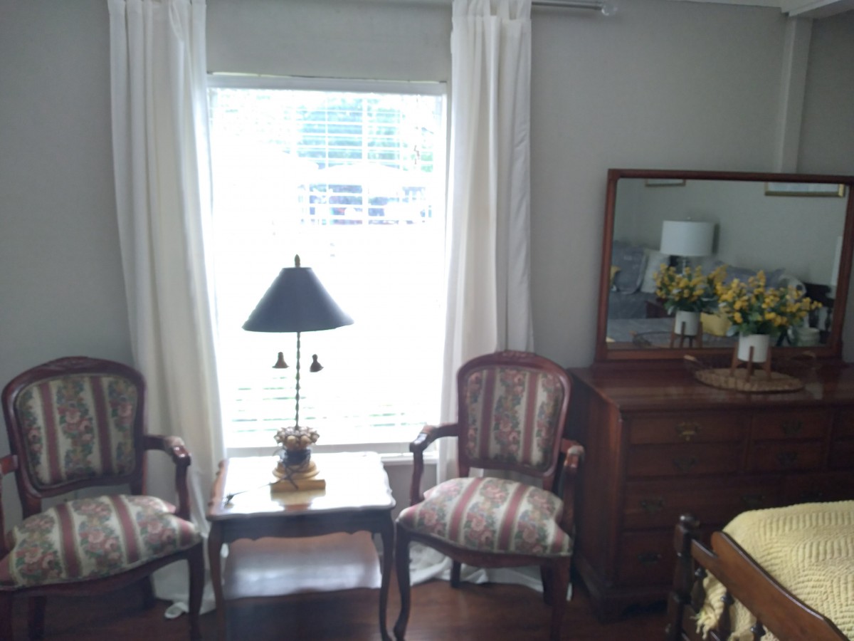 A cozy living room corner featuring two chairs, a small table with a lamp, and a window with curtains.