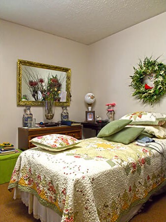 A cozy bedroom with a decorative wreath and a floral quilt on the bed.
