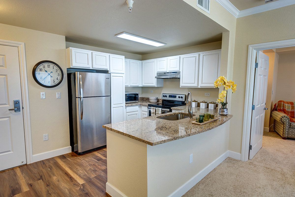A modern kitchen with stainless steel appliances and granite countertops, featuring white cabinets and a hardwood floor.