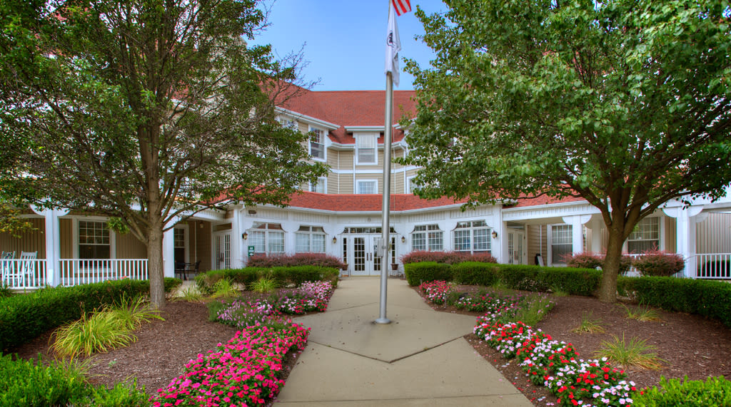 A well-maintained building fronted by a landscaped garden with colorful flowers and a pathway, featuring a flagpole at the center.