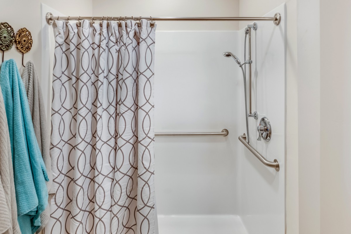 A bathroom shower area with a patterned curtain and safety grab bars.