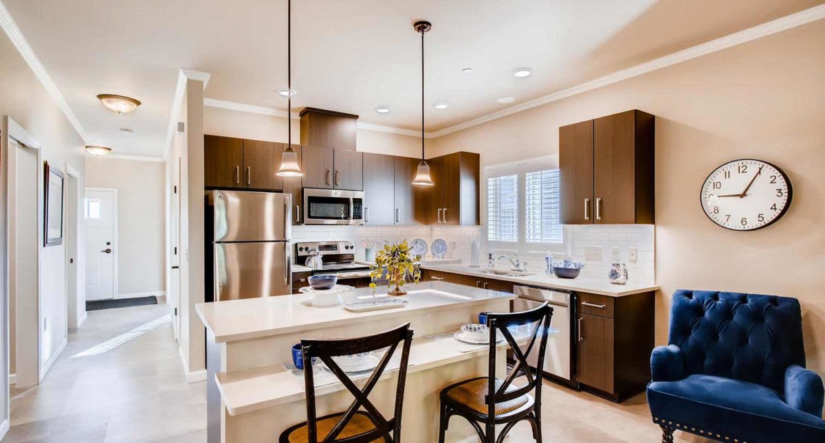 A modern kitchen with stainless steel appliances and a central island, featuring pendant lighting and bar stools.