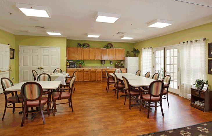 A dining area with multiple tables and chairs, featuring a kitchen at the back.