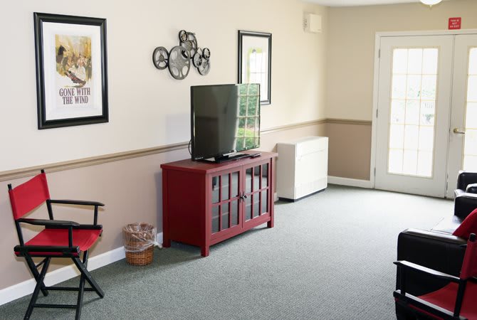 A cozy living room featuring a television on a red cabinet, wall artwork, and seating.