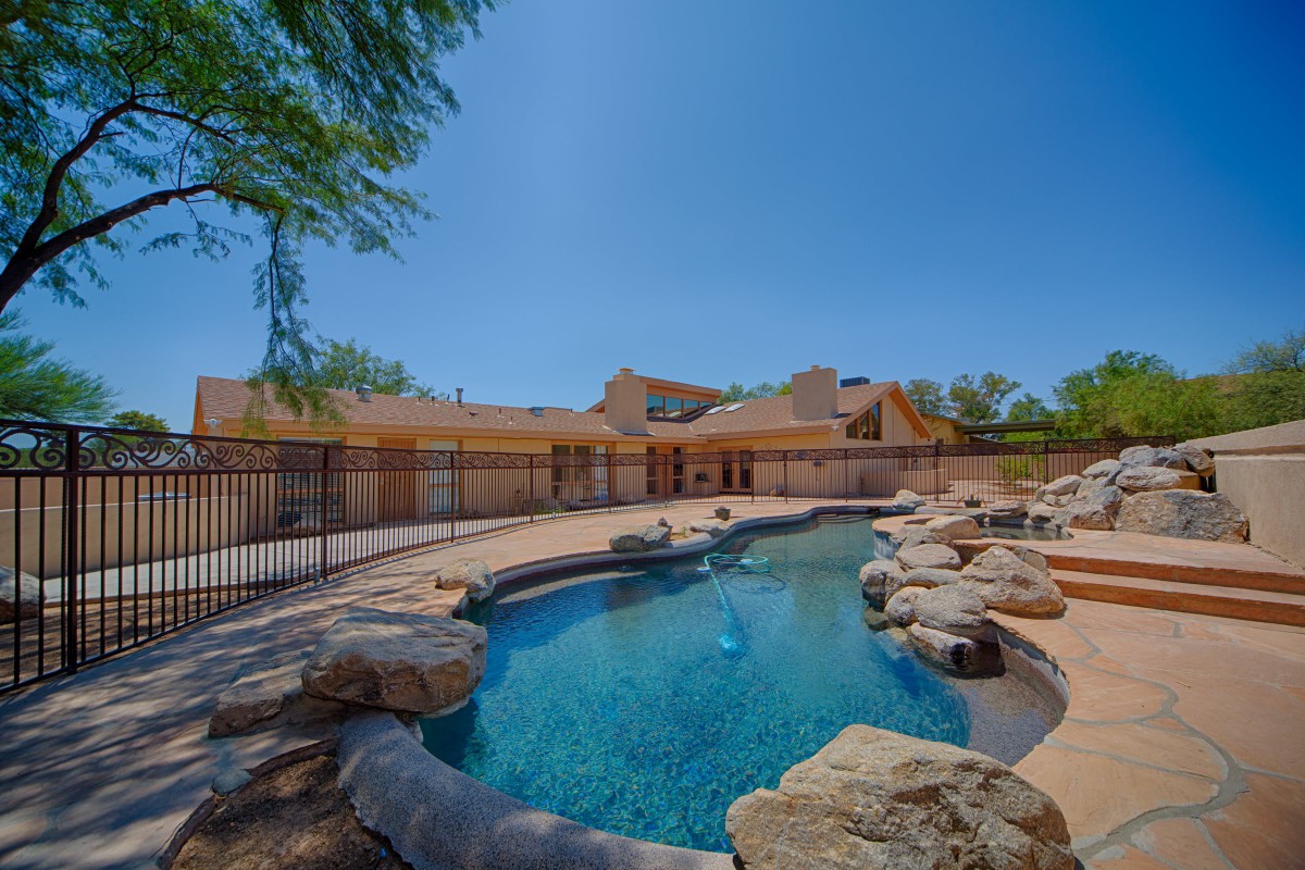 A serene backyard with a swimming pool surrounded by rock landscaping and clear blue skies on a sunny day.