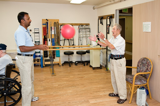 A physical therapy session where an elderly person practices catching a ball with the assistance of a therapist.
