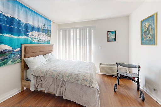 A bright and inviting bedroom featuring a cozy bed, window blinds, and wall art.
