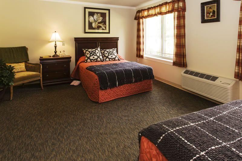 A cozy hotel room with two double beds, a lamp on the nightstand, and a large window providing natural light.