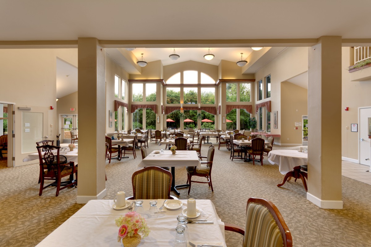 A spacious and elegant dining room with large windows, featuring neatly arranged tables and chairs.