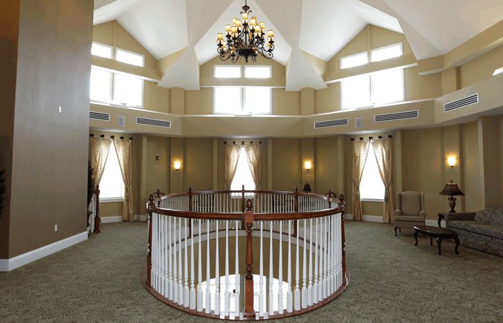 A luxurious interior with a chandelier hanging from a high ceiling, surrounded by large windows and a circular balcony with white railings.